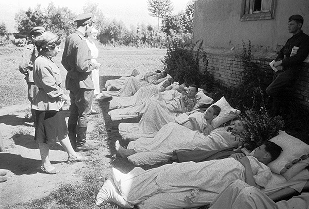 Константин Симонов читает свои стихи раненым бойцам, лежащим в тени дома на земле. Орловско-Курское направление