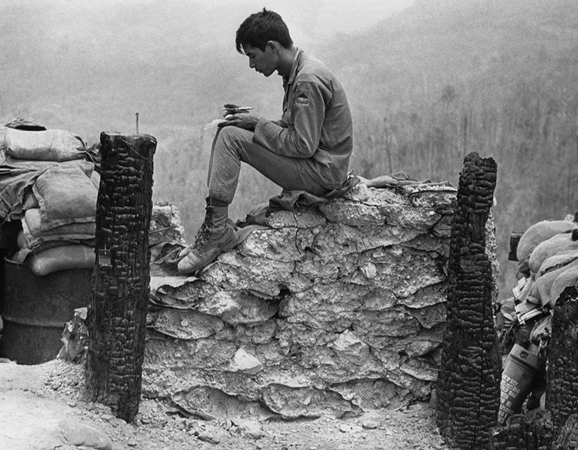 Южновьетнамский солдат использует несколько минут уединения, чтобы написать письмо, сидя на мешках с песком.