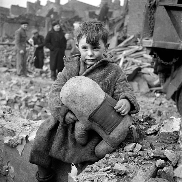 Одинокий брошенный мальчик с игрушечным животным в руках сидит в окружении руин. Снимок сделан после бомбардировки Лондона в 1945 году.