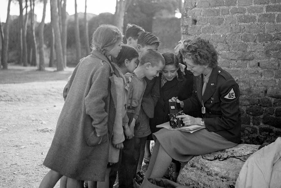 Фотограф Тони Фрисселл сидит с камерой на коленях, окруженная несколькими детьми. Точное место съемки неизвестно. Европа, 1945 год.
