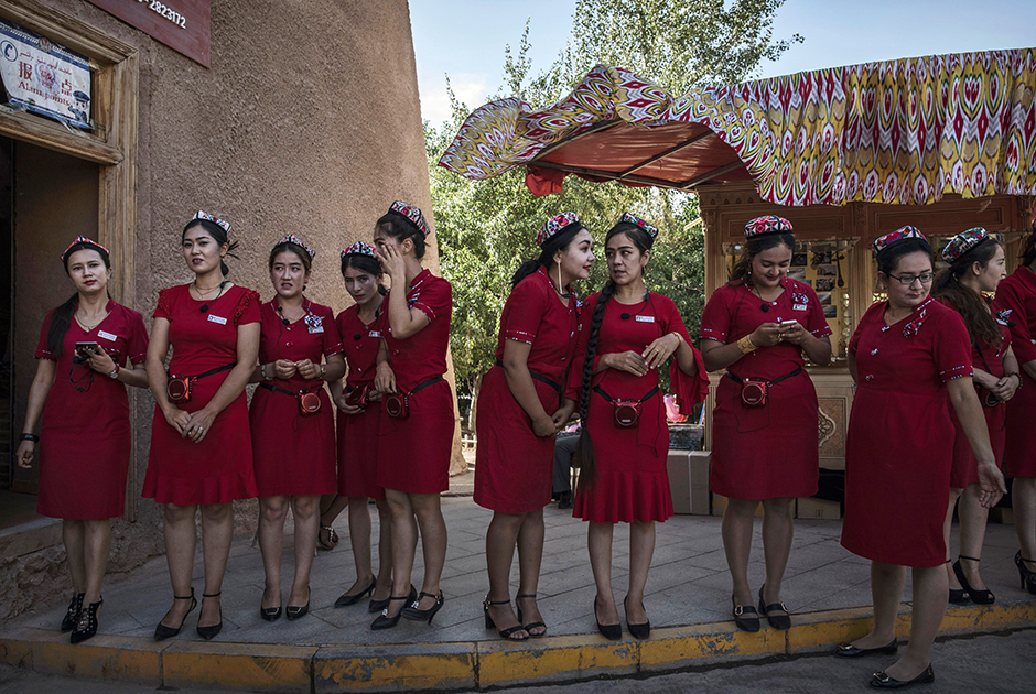 Гиды в национальных головных уборах выстроились в ожидании прибытия туристических групп. Несмотря на то что большинство уйгуров почти не говорит на китайском, гидов набирают среди местного населения.