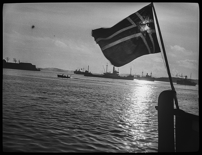 Норвежский флаг на борту судна, на фоне немецких кораблей и патрульного катера. Норвегия, 1940 год.
