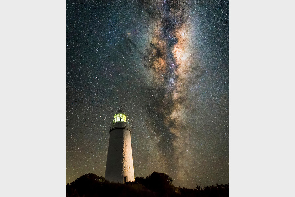 Млечный Путь над маяком в Тасмании. Этот снимок — один из серии изображений, полученных в ходе покадровой съемки. На нем можно увидеть самого фотографа, который поднялся на маяк.