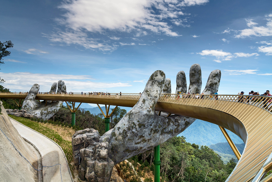Пешеходный мост в Аннамских горах открылся для туристов в июне 2018 года. Огромные каменные руки, держащие золотую конструкцию, на самом деле сделаны вовсе не из камня. Это каркас, покрытый стальной сеткой. Дизайнеры воплотили эту идею, чтобы создать видимость древности.