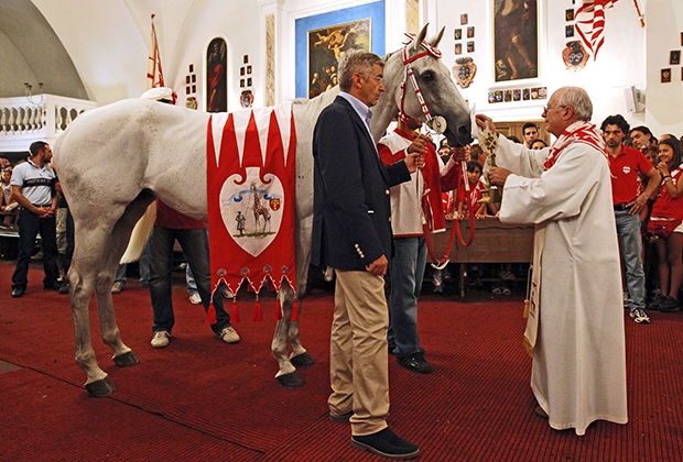 Традиция благословлять лошадь и жокея утром перед гонкой прямо в главной церкви контрады соблюдается до сих пор, несмотря на возмущение верующих из других частей Италии. На фото церемония в контраде «Жирафа» (Giraffa) 16 августа 2011 года. 