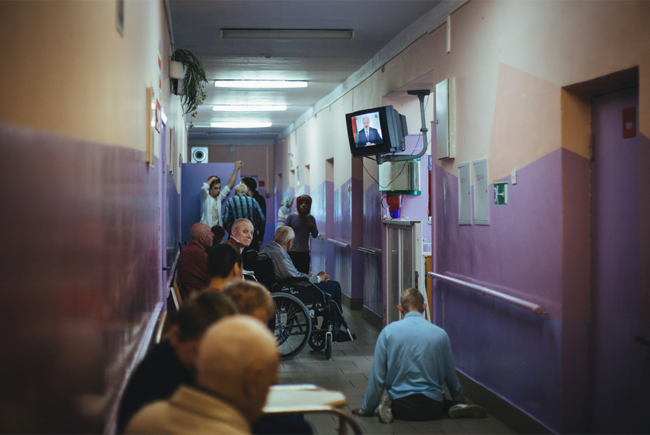 Интерьер психоневрологического интерната для престарелых и инвалидов № 3. Пациенты смотрят выпуск новостей в коридоре.