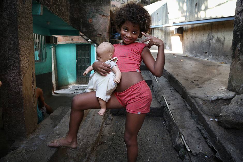 Девочка из фавелы Росинья в Рио-де-Жанейро.Трущобные кварталы находятся совсем рядом с фешенебельными районами, сюда довольно часто заходят туристы — любители острых ощущений. Иногда они их находят — фавела не полностью подконтрольна полиции. Официально население Росиньи перевалило за 70 тысяч человек, неофициально — называют разные цифры, вплоть до 200 тысяч.