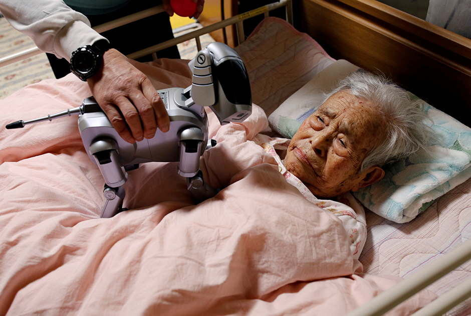 Йоичи Судзуки показывает своей прикованной к постели матери собаку-робота «Айбо». Робот, который «испытывает» эмоции в зависимости от ситуации, помог отцу Судзуки реабилитироваться после болезни.

