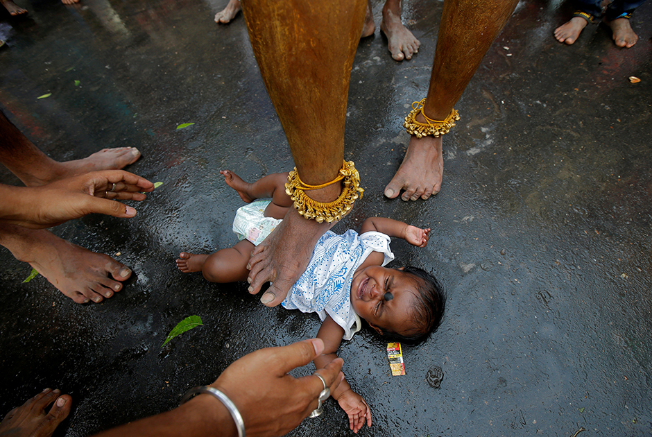 Индийский брахман прикасается ногой к ребенку. Таким образом он благословляет малыша во время праздника, посвященного богине-матери Мариамман.


