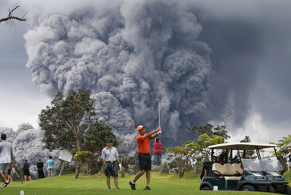 Увлеченные игроки в гольф в Гавайском вулканическом национальном парке не замечают, что активный вулкан Килауэа выплюнул в воздух облако пепла. 15 мая 2018 года.