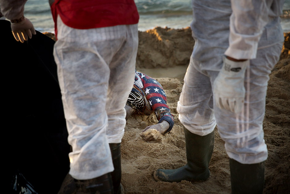 Сотрудники ливийского отделения Международного движения Красного Креста и Красного Полумесяца вытаскивают из песка безжизненное тело утонувшего мигранта. В течение нескольких дней после того, как у восточного побережья Триполи затонула лодка с мигрантами, волонтеры обнаружили 11 тел.