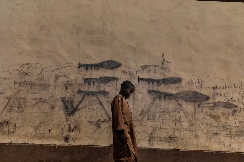 Мальчик-сирота у стены, на которой изображена атака противотанковых гранатометов в городе Бол в Чаде. Номинация «Окружающая среда».