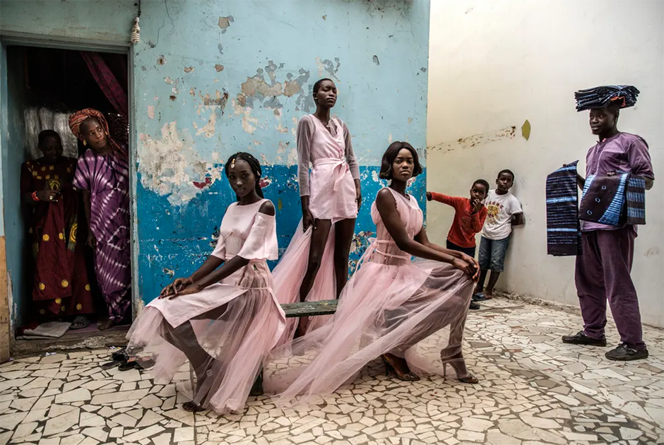 Любопытные жители и уличный торговец наблюдают за тем, как три модели на улице Дакара позируют в нарядах сенегальского дизайнера. Номинация «Одиночные портреты».

