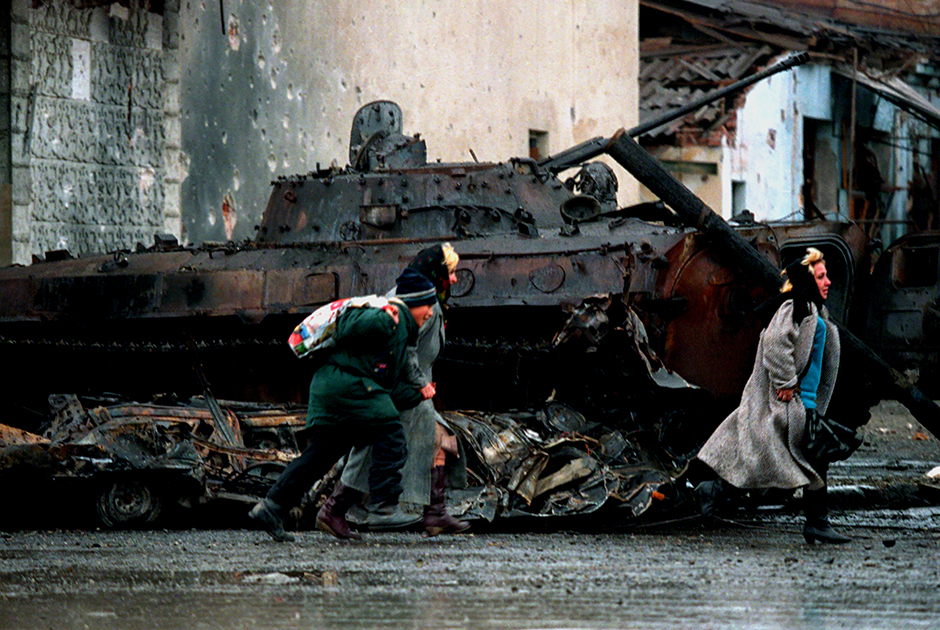 Мирные жители Чечни бегут из центра Грозного во время боевых действий 4 января 1995 года. За ними — уничтоженная БМП российской армии.