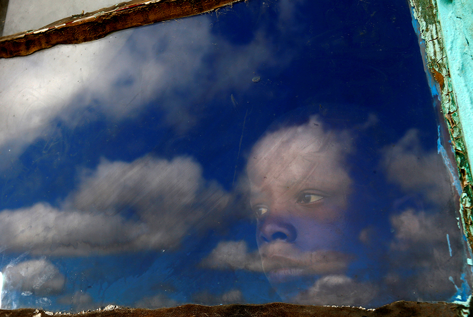 Мальчик по имени Анда смотрит из окна своей хижины на место захоронения бывшего президента ЮАР Нельсона Манделы в родовой деревне Цгуну 15 декабря 2013 года.