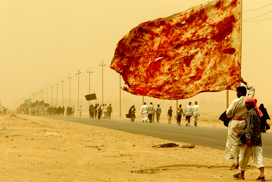 Иракский шиит совершает вместе с сотнями тысяч религиозных жителей Ирака паломничество в священный город Кербела. Он несет флаг, раскрашенный кровью мужчин, — они умышленно ранили себя, чтобы продемонстрировать свое уважение и любовь к покойному имаму Хусейну. 23 апреля 2003 года, на сороковой день после его смерти, миллионы верующих почтили его память.