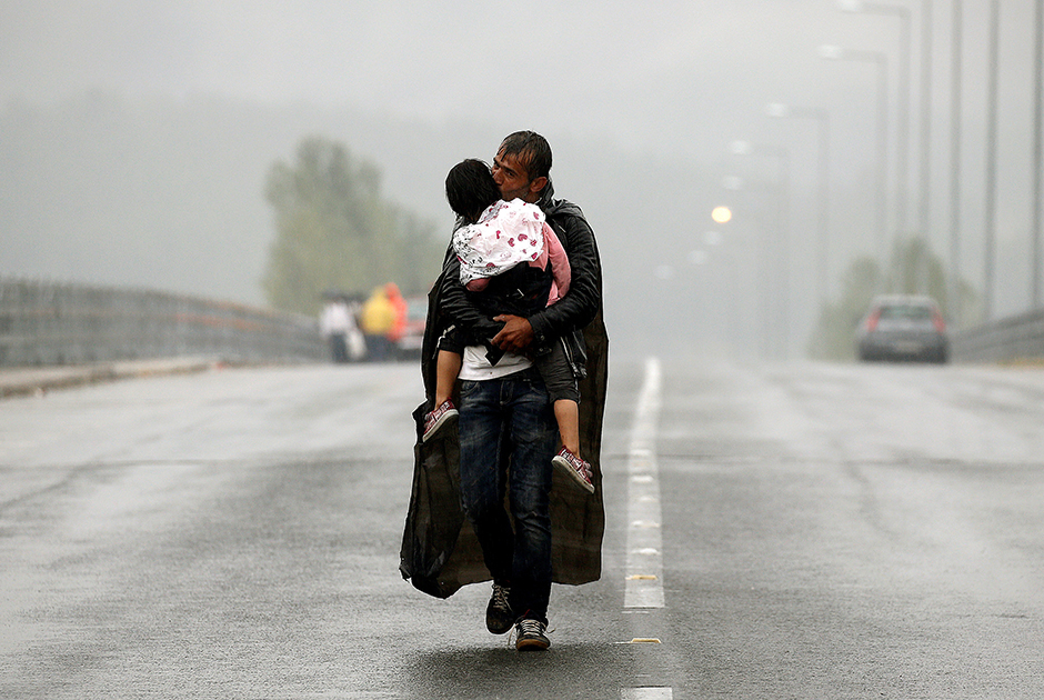 Сирийский беженец целует свою дочь. Они идут сквозь ливень к границе Греции с Македонией. Фотография сделана 10 сентября 2015 года.