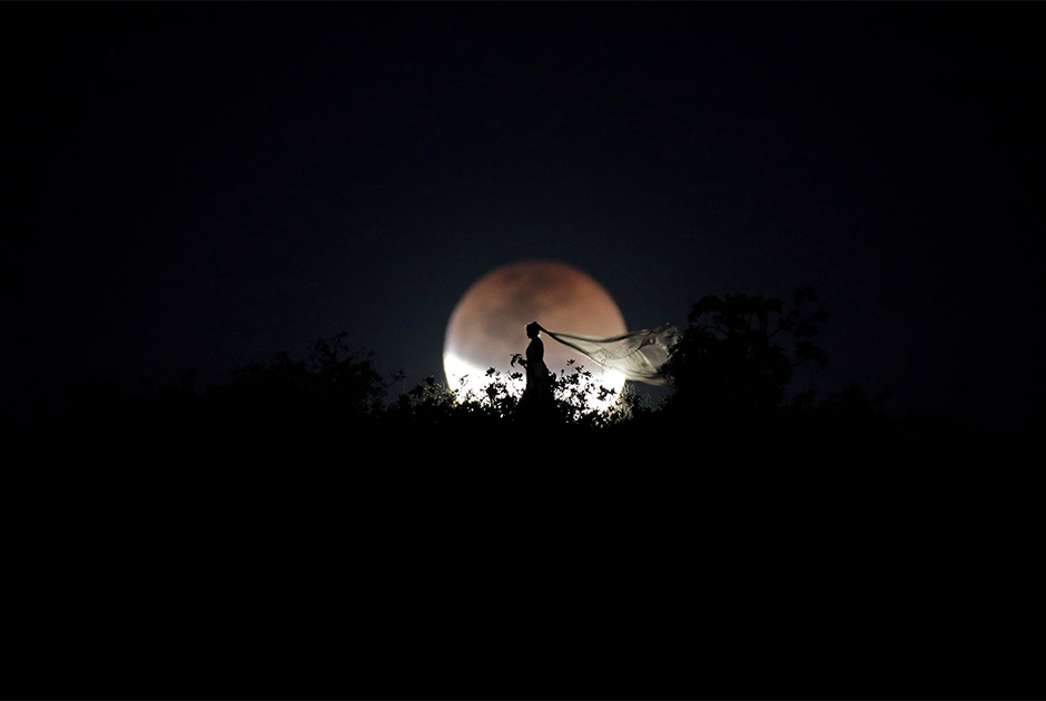 Тема мигрантов — не единственное, что интересовало Уэсли Марселино в минувшем году. Фотограф следил за полным лунным затмением, которое наблюдалось в Южном полушарии 27 июля. На фото — бразильская невеста позирует на фоне Луны во время астрономического явления. 
