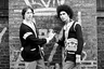Два участника банды Latin Kings в боевых свитерах группировки стоят напротив стены с эмблемой банды. Фото из коллекции Роберта Рихака. 