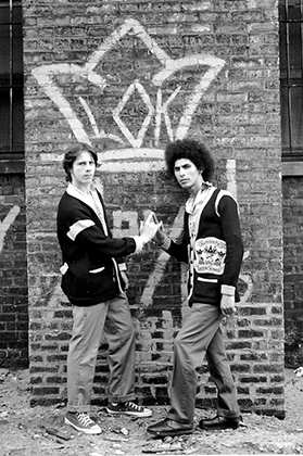 Два участника банды Latin Kings в боевых свитерах группировки стоят напротив стены с эмблемой банды. Фото из коллекции Роберта Рихака. 
