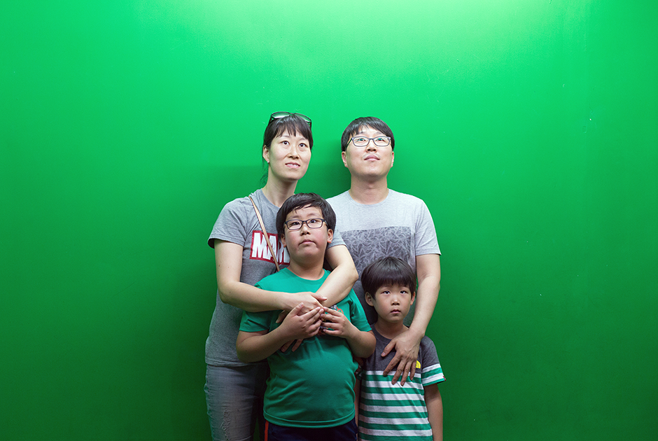Корейская семья фотографируется на память в пусанском океанариуме. Зеленый экран поменяют на рыб и морскую живность в фоторедакторе. 