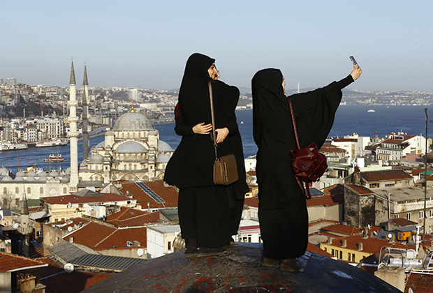 Молодые девушки, одетые в традиционные черные накидки абайи, позируют на фоне мечети на берегу Босфора в Стамбуле. В последние годы на улицах больших городов появляется все больше девушек в традиционной одежде. 