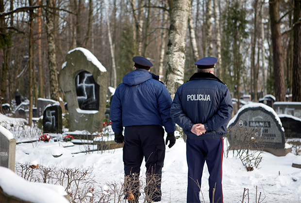 Офицеры полиции рассматривают оскверненные нацистской символикой могилы на Еврейском кладбище в Риге. Декабрь 2010 года