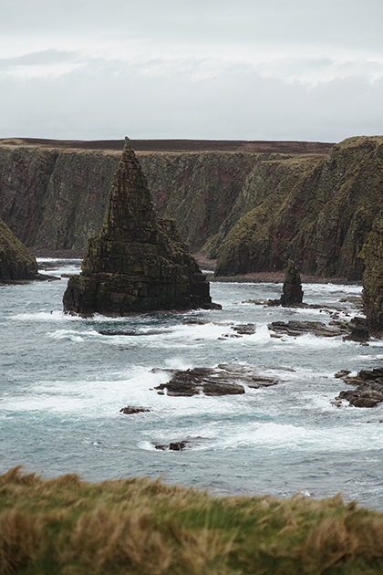 Если взглянуть на карту Шотландии и приглядеться к очертаниям ее побережья, создается впечатление, будто кто-то долго и небрежно рвал его на куски. Так же оно выглядит и в жизни. Самая северная точка материковой Шотландии Duncansby Head — яркий тому пример. Мрачные клифы, покрытые толстым ковром мха, и острые скалы, изборозжденные трещинами от суровых северных ветров, формируют эталонный шотландский пейзаж, притягивающий туристов со всего мира.