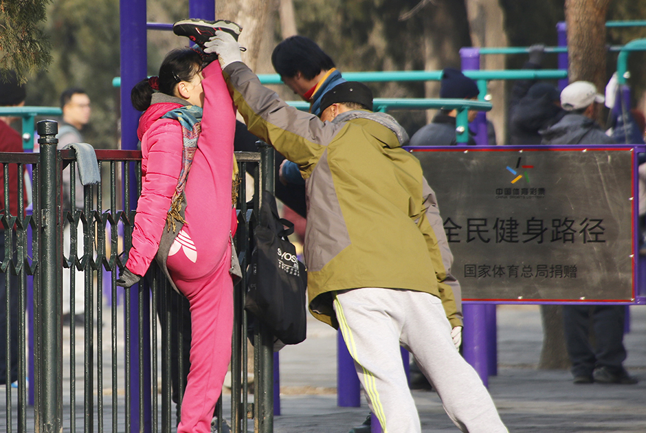 Китайцы любят заниматься йогой и гимнастикой прямо на улице. На фото мужчина помогает девушке выполнить вертикальный шпагат в одном из парков Пекина. 