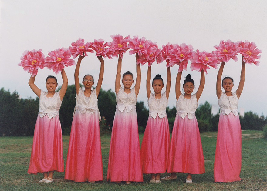 Девочки в традиционных китайских вечерних платьях готовятся выступить с танцем в честь региональных властей.