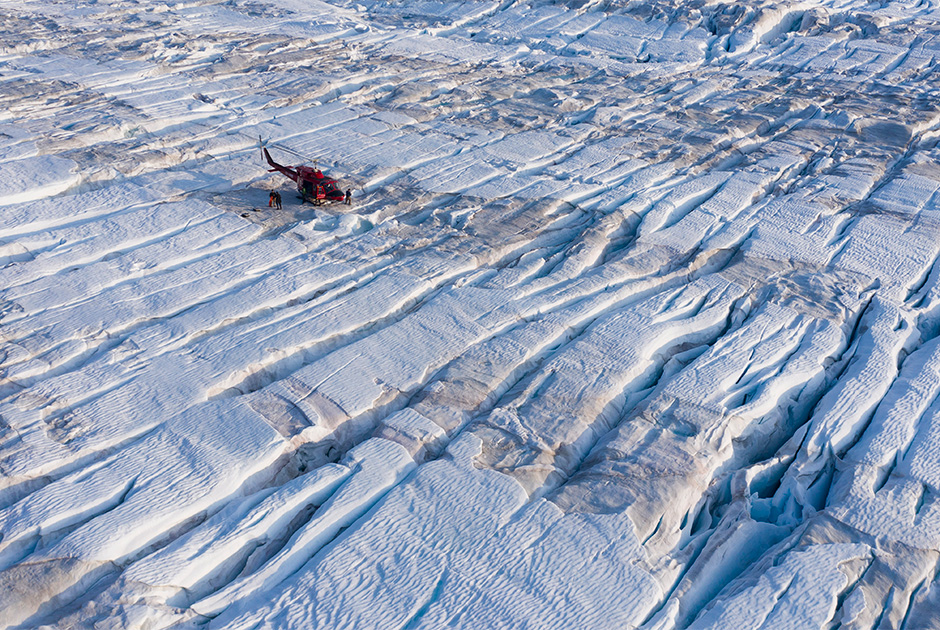 Вертолет ученых стоит на льду, пока исследователи устанавливают радар и GPS-антенны.