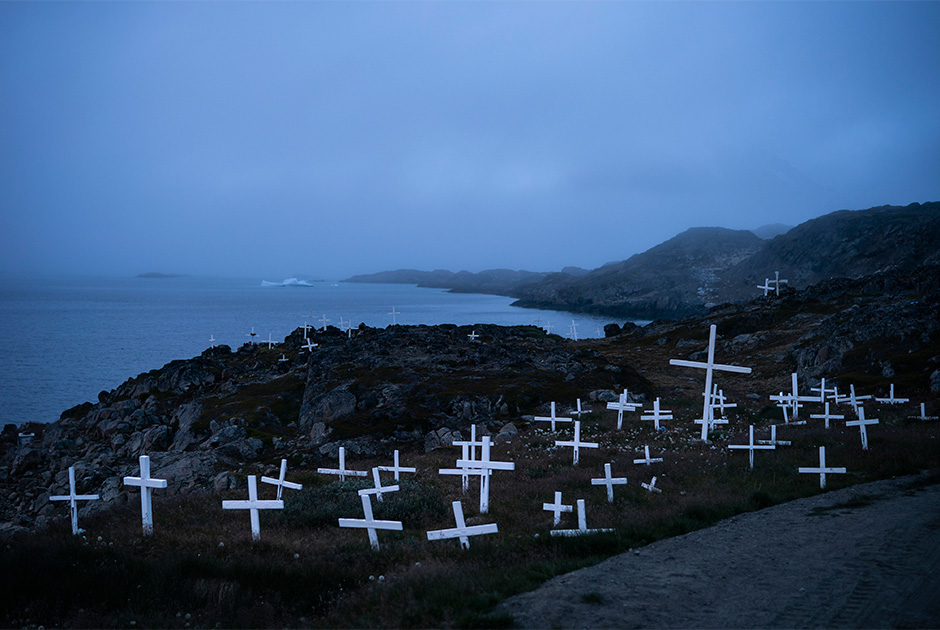 Кладбище в Кулусуке и айсберг на заднем фоне. Один из жителей деревни Мугу Утуак (Mugu Utuaq) утверждает, что зима, которая тянулась 10 месяцев, когда он был ребенком, сейчас длится всего 5 месяцев.