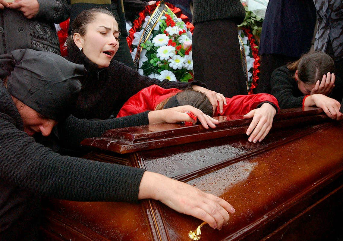 BESLAN, RUSSIA - SEPTEMBER 6: Family and friends of those killed in the school hostage crisis cry over the coffin of a loved one during a mass funeral in the rain September 6, 2004 in Beslan, southern Russia. More than 350 people died after Chechen militant hostage-takers and Russian forces began a firefight that ended violently for more than 1200 held captive inside the school for three days. (Photo by Scott Peterson/Getty Images)