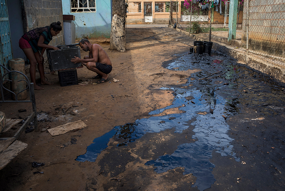 Отец и дочь устанавливают кондиционер на улице. Возле их дома в Кабимасе подтекает нефтепровод