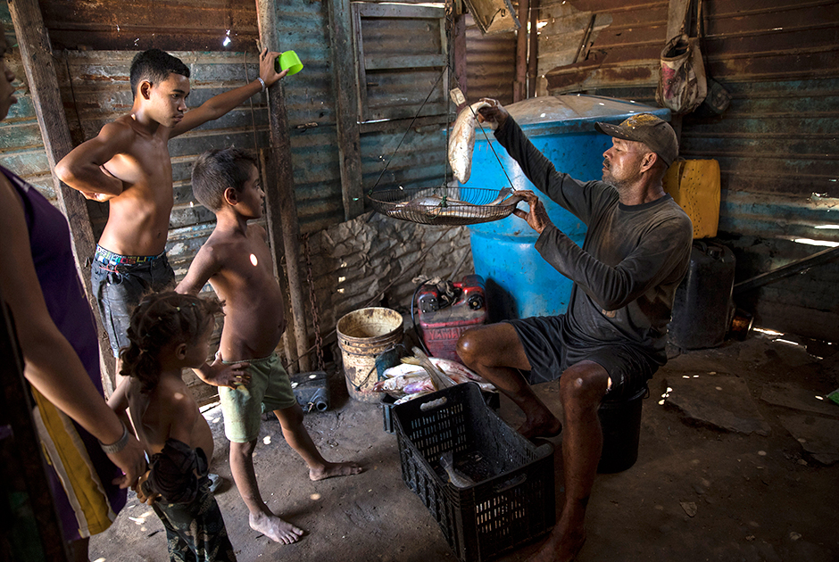 Рыбак Алехандро в испачканной нефтью одежде взвешивает улов после рабочего дня на озере