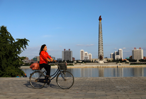 Женщина на велосипеде на фоне монумента идеям чучхе в Пхеньяне
