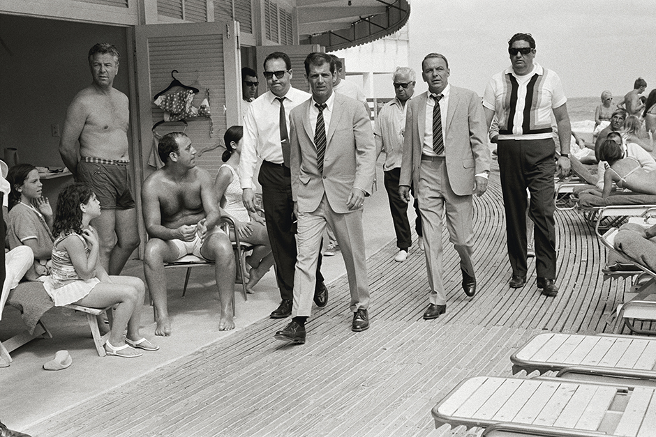 Американский актер и певец Фрэнк Синатра (в центре) с дублером (справа) в окружении телохранителей на пляже в Майами. Снимок сделан во время съемок фильма «Леди в цементе» в 1968 году.