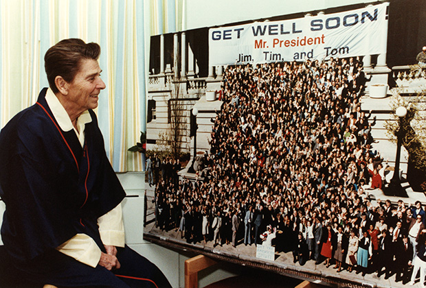 Раненный Рейган рассматривает гигантскую открытку с пожеланием скорейшего выздоровления после покушения 30 марта 1981 года, через два месяца после его вступления в должность