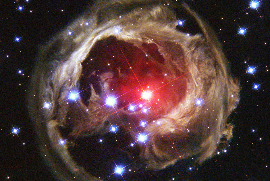 Вихри пыли, вращающиеся вокруг триллионов километров межзвездного пространства в виде расширяющегося ореола света вокруг далекой звезды, названной «V838 Единорога», освещают гигантское облако. Сияние исходит от красной супергигантской звезды в центре изображения, которая излучала подобный вспышке импульс света. На снимке показан прогресс, достигнутый световым импульсом после двух лет путешествия от звезды во всех направлениях, запечатленный «Хабблом» 8 февраля 2004 года. «V838 Единорога» расположена примерно в 20 тысячах световых лет от Земли в направлении созвездия «Единорога», на внешней границе Млечного Пути.
