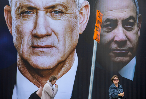 Люди на фоне плаката оппозиции. На первом плане — Бени Ганц, на втором — Нетаньяху