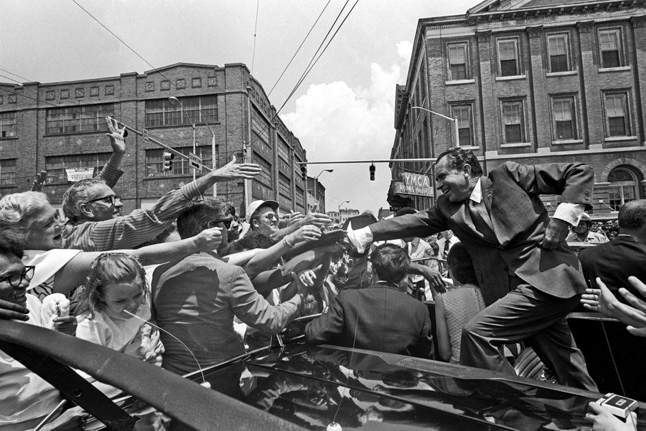 Никсон стоит на бампере своего автомобиля и протягивает руку толпе для рукопожатий, 1971 год