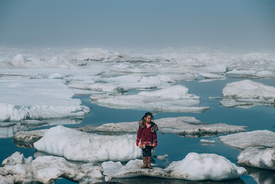 11-летняя инупиатская девочка стоит на льдине на берегу Северного Ледовитого океана, на мысе Барроу (Аляска). Аномальное таяние арктических льдов является одним из множества последствий глобального потепления, влияющих на жизнь человека и диких животных. В последние годы плавучий лед встречается все дальше от линии побережья, так как он начинает таять все раньше и быстрее. Таяние ледников привело к массовой миграции моржей и морских львов в 2015 году. Инупиатам становится все сложнее охотиться на животных.

