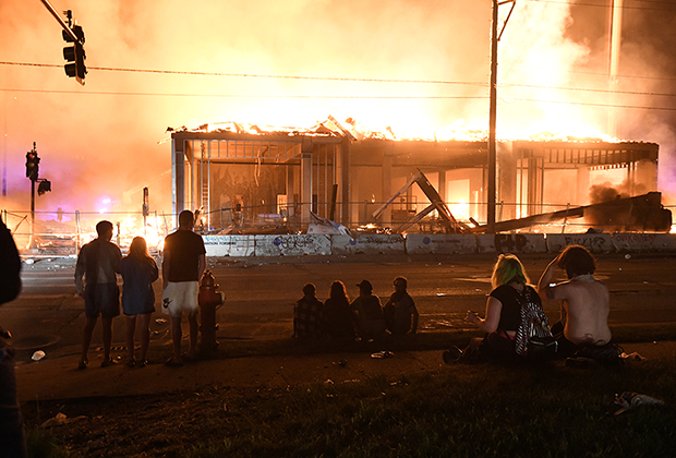 Демонстранты смотрят на горящую стройку возле полицейского участка в Миннеаполисе