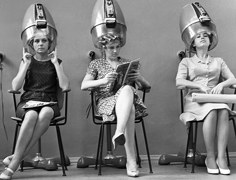 Здесь показан символ советских парикмахерских — ряды сушуаров. Женщины на снимке делают завивку волос, которая была еще одной крайне востребованной услугой благодаря веяниям моды того времени. Кудри создавались с помощью бигуди, они могли быть горячими либо холодными. А если в салоне заканчивались укладочные средства, парикмахеры пускали в ход пиво — смачивали им волосы перед завивкой.
 
 
Часто женщины делали так называемую «шестимесячную» химическую завивку. Такая прическа не боялась воды и солнца. 
