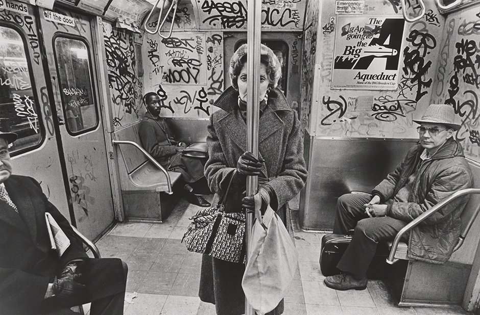 Один из самых выразительных снимков в карьере фотографа, режиссера-документалиста и саксофониста Ричарда Сэндлера запечатлевает типичную картину в нью-йоркском метро середины 1980-х — которое было печально известно как плачевным состоянием, так и своей небезопасностью для пассажиров. Ветка СС (сейчас переименованная в С) была единственной, охватывавшей сразу четыре городских боро, — она следовала из Куинса через Бруклин и Манхэттен в Бронкс — и поэтому в ее вагонах можно было встретить публику с самых разных ступеней классовой лестницы.