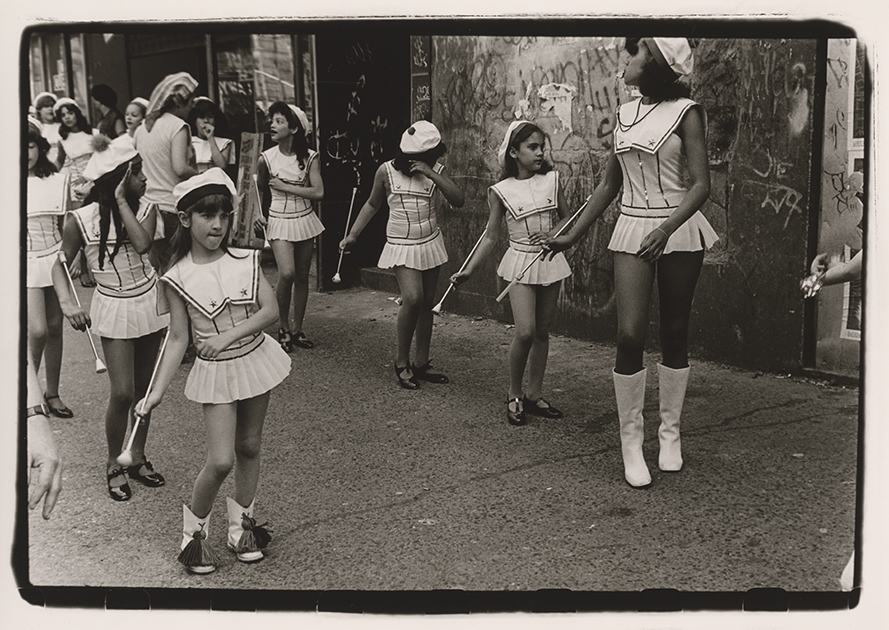 Еще один живой классик нью-йоркской фотографии (причем не только уличной, но и портретной) Харви Вонг на этом снимке увековечил такую неотъемлемую часть манхэттенской жизни, как большие, массовые парады: именно к выступлению в одном из них готовятся в кадре девочки с жезлами. В последние годы уходящая нью-йоркская натура стала одной из центральных тем для Вонга — как в книгах фотографий, так и в короткометражных фильмах, самый пронзительный из которых называется «Последний ньюйоркец».
