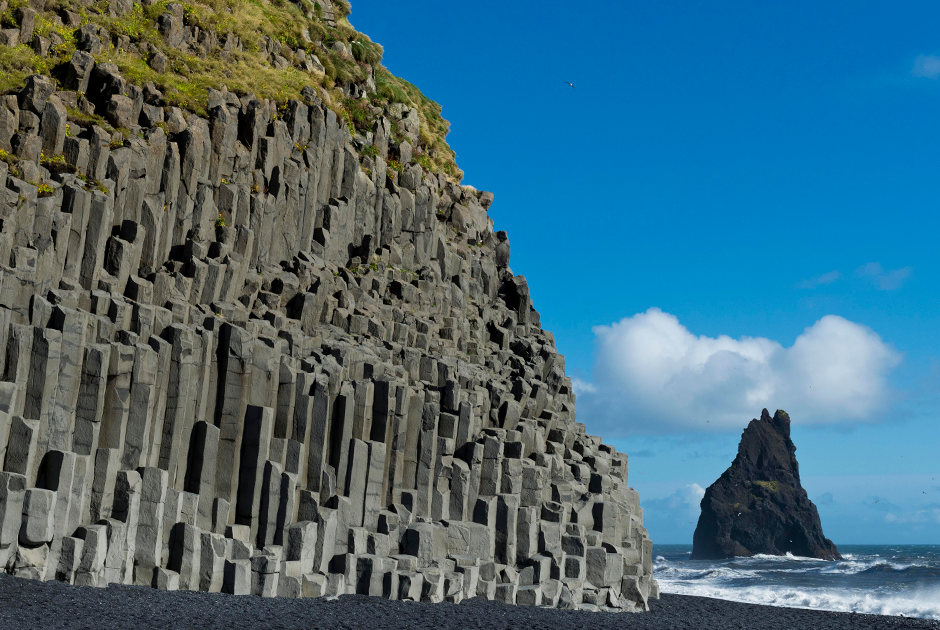 Сотни каменных столбов как будто выросли из земли и неподвижно застыли на берегу океана — базальтовые колонны Рейнисдрангар в Исландии, как и окружающий их сыпучий, черный словно смола песок, образовались из-за вулканической активности. Когда-то здесь навсегда остыли густые потоки лавы, а ее сплошные куски раскололись на отдельные элементы в форме загадочных шестигранников.