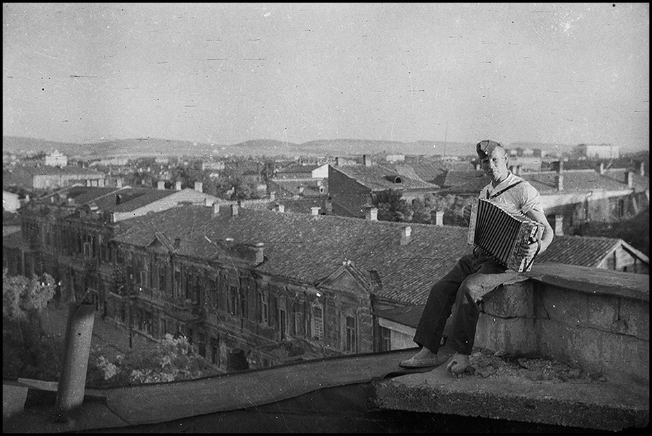 Немецкий солдат играет на гармошке на крыше одного из домов. 1941-42 гг.