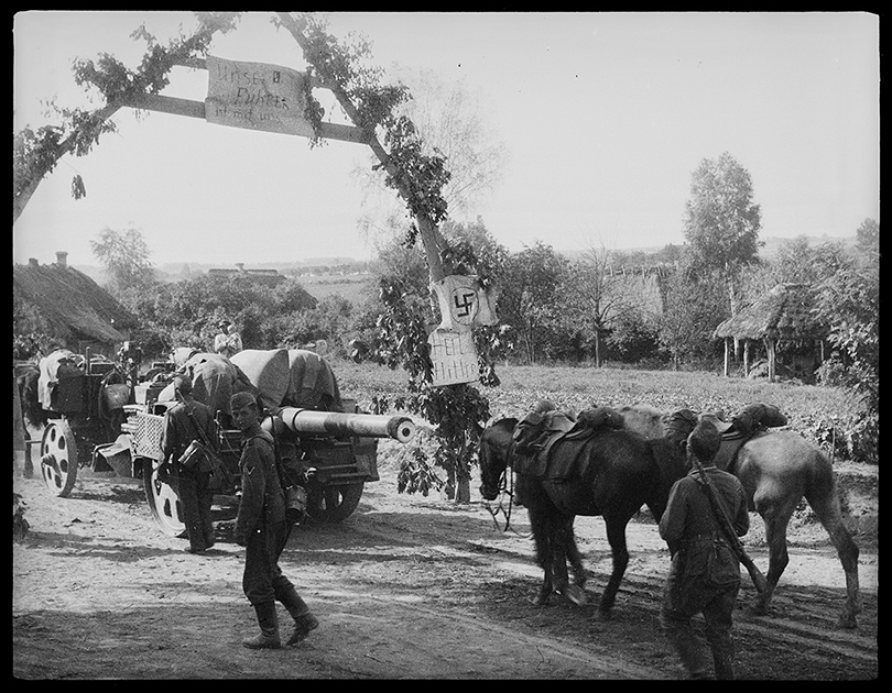 Немецкие войска входят в украинскую деревню. Самодельная деревянная арка украшена нацистской свастикой и приветственными плакатами «Heil Hitler» («Да здравствует Гитлер») и «Unser Fuhrer ist mit uns» («Наш фюрер с нами»). Июль 1941 года.