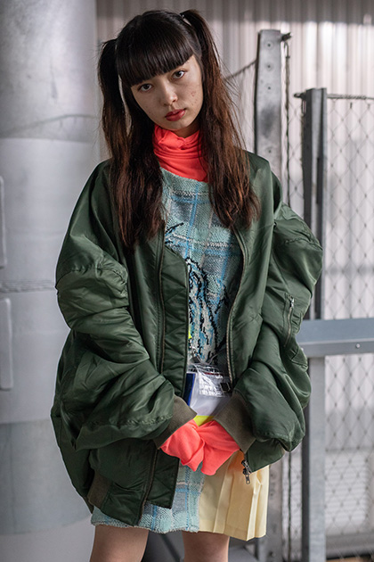 Еще одна гостья токийских модных шоу показала идеальный образ нынешнего осеннего сезона, детали которого позаимствованы у эстетики 1990-х годов. Девушка появилась на мероприятиях в розовой неоновой водолазке в сочетании с клетчатым платьем и темно-зеленой курткой-бомбером, дополнив свой наряд сумкой на кислотно-желтом ремне. 

